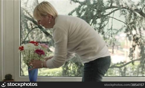 Senior caucasian woman with bunch of flowers in living room at home. Dolly shot