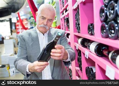 senior checking wine bottle at the supermarket