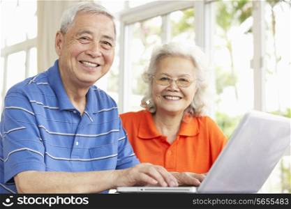 Senior Chinese Couple Sitting At Desk Using Laptop At Home