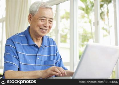 Senior Chinese Man Sitting At Desk Using Laptop At Home