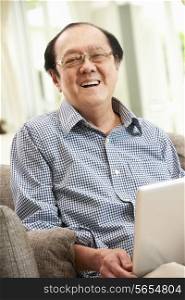 Senior Chinese Man Using Laptop Whilst Relaxing On Sofa At Home