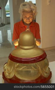 Senior Chinese Woman Praying To Statue Of Buddha At Home