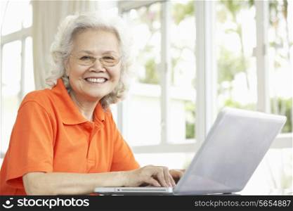 Senior Chinese Woman Sitting At Desk Using Laptop At Home