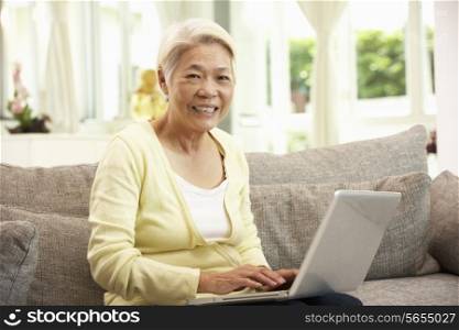 Senior Chinese Woman Using Laptop Whilst Relaxing On Sofa At Home
