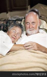 Senior couple asleep in bed, holding hands. Vertical view.