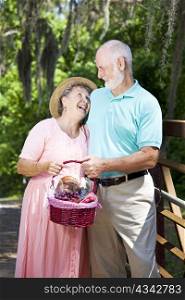 Senior couple carrying a picnic basket and laughing together.