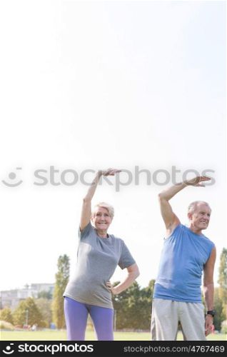 Senior couple doing stretching exercise in park against sky