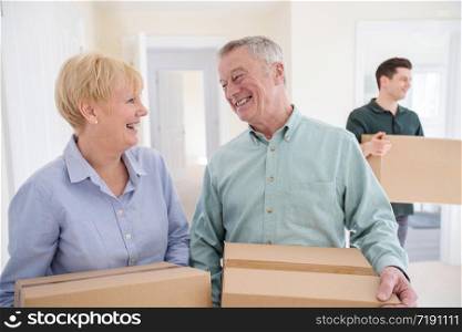 Senior Couple Downsizing In Retirement Carrying Boxes Into New Home On Moving Day With Removal Man Helping