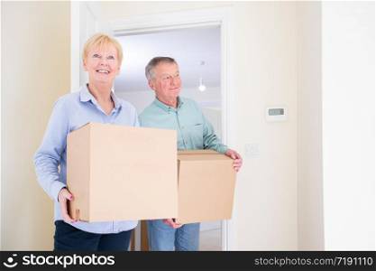 Senior Couple Downsizing In Retirement Carrying Boxes Into New Home On Moving Day