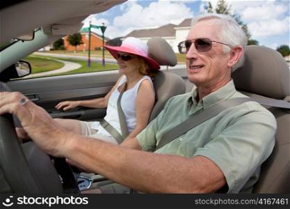 Senior Couple Driving Convertible Car Wearing Sunglasses