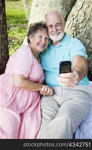 Senior couple e-mailing a picture of themselves to their kids, using a cellphone.