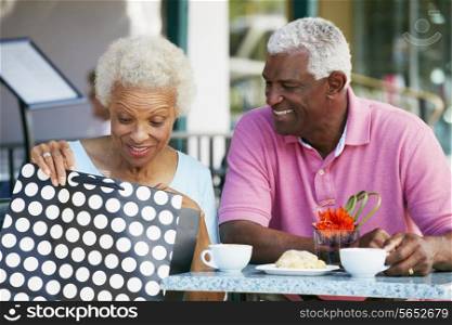Senior Couple Enjoying Snack At Outdoor Cafe After Shopping
