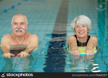 senior couple exercising with floats in swimming pool
