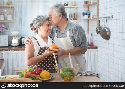 Senior couple having fun in kitchen with healthy food - Retired people cooking meal at home with man and woman preparing lunch with bio vegetables - Happy elderly concept with mature funny pensioner.