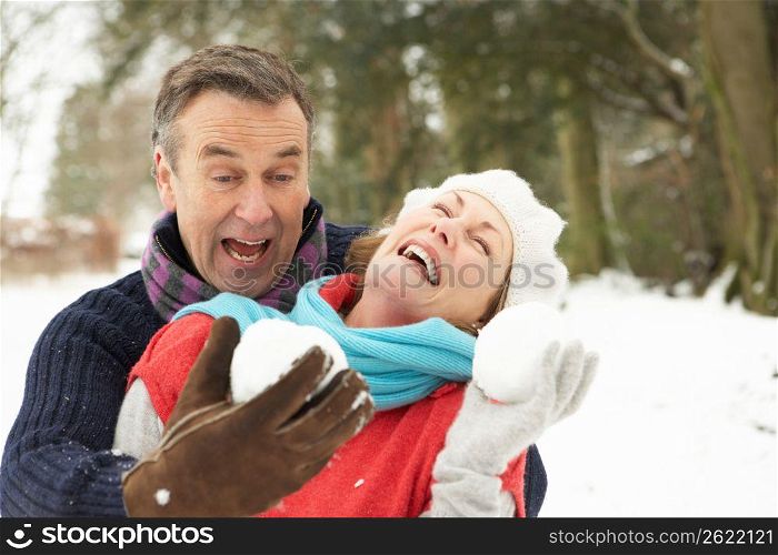 Senior Couple Having Snowball Fight In Snowy Woodland
