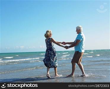 Senior couple holding hands on beach while dancing side view