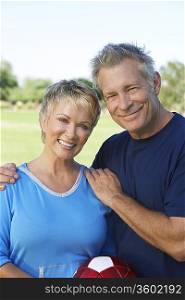 Senior couple holding soccer ball in park, portrait