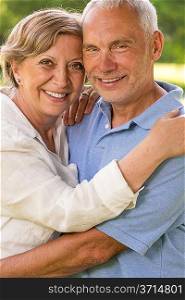 Senior couple hugging and smiling in park looking at camera