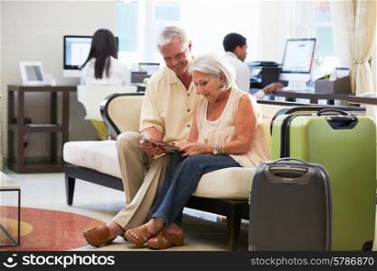 Senior Couple In Hotel Lobby Looking At Digital Tablet