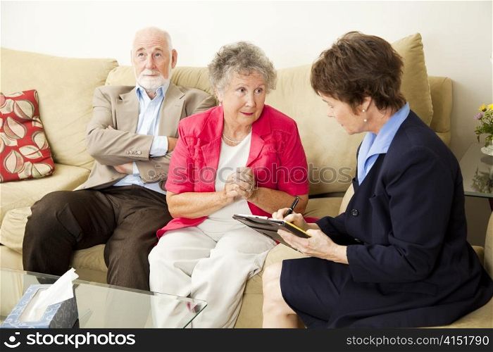 Senior couple in marriage counseling. The wife talks while the counselor takes notes.