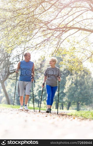 Senior couple in sportswear walking with poles on footpath