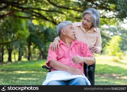 Senior couple in the park and wife taking care of a husband in a wheelchair a patient with paralysis, with his wife comforting and encouraging each other. Retirement health insurance concept.