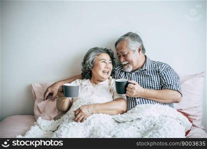 Senior couple laughing while drinking coffee in bedroom