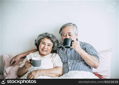 Senior couple laughing while drinking coffee in bedroom