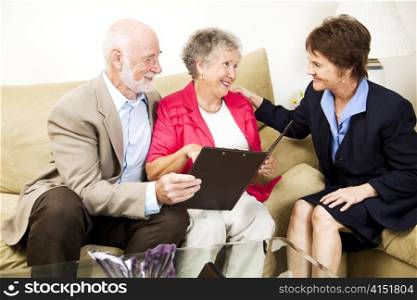 Senior couple listens to a saleswoman or financial consultant in their home.