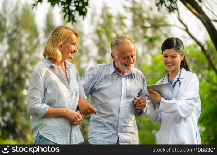 Senior couple man and woman talking to young nurse or caregiver in the park. Mature people healthcare and medical staff service concept.