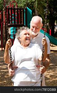 Senior couple on a playground, swinging on the swingset.