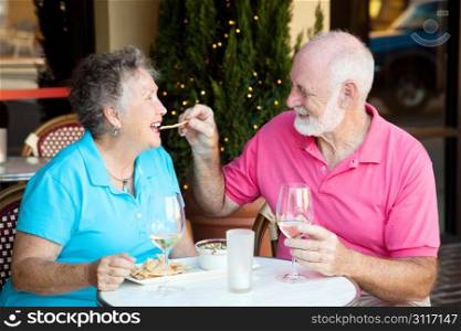 Senior couple on romantic lunch or dinner date. He&rsquo;s feeding her the appetizer by hand.