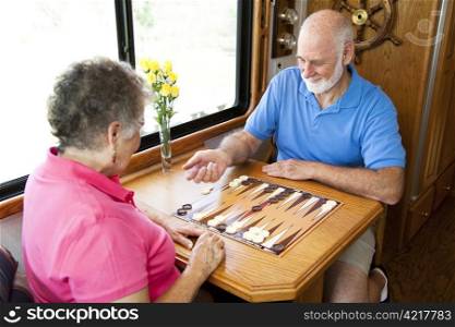 Senior couple on vacation playing backgammon in their motor home. Motion blur on the man&rsquo;s hand as he shakes the dice.