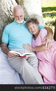 Senior couple outdoors, reading a book together.