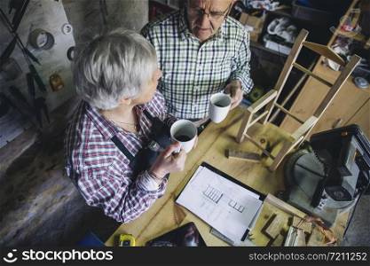 Senior couple pausing for coffee in their carpentry workshop. Senior couple in their carpentry