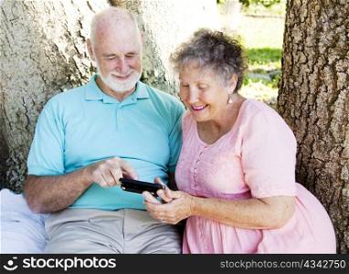 Senior couple reading a text message together, outdoors under a tree.
