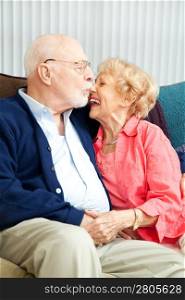 Senior couple relaxing at home, she&rsquo;s laughing as he kisses her nose.