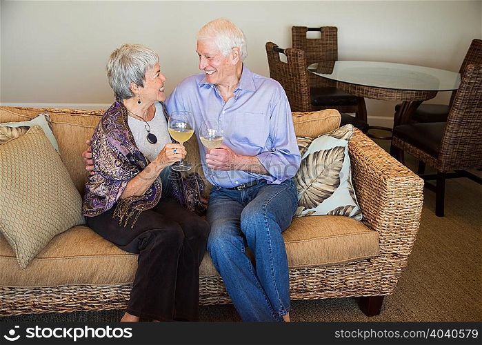 Senior couple relaxing on sofa, holding glass of wine, smiling