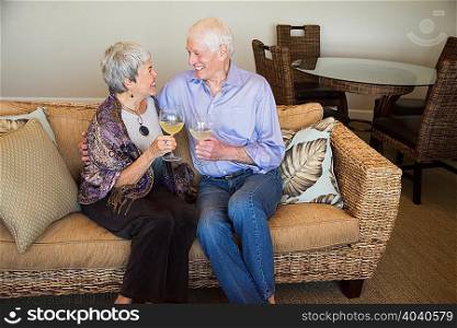 Senior couple relaxing on sofa, holding glass of wine, smiling
