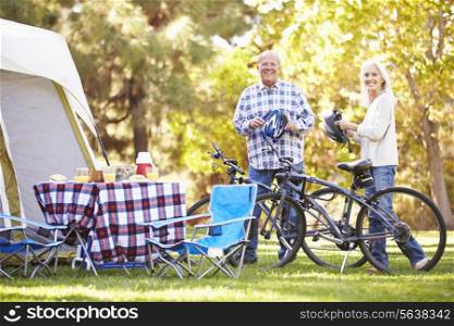 Senior Couple Riding Bikes On Camping Holiday In Countryside