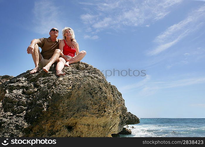 Senior couple sat on a rock by the sea