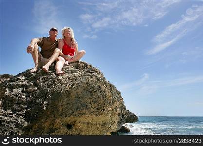 Senior couple sat on a rock by the sea