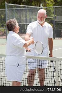 Senior couple shakes hands over the net on the tennis court.