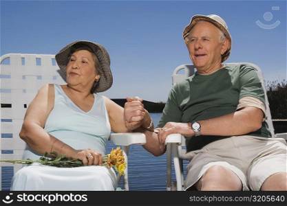Senior couple sitting at the lakeside with holding hands of each other