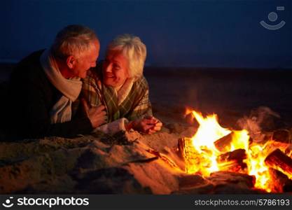 Senior Couple Sitting By Fire On Winter Beach
