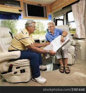 Senior couple sitting in RV looking at map and smiling.
