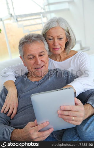 Senior couple sitting in sofa with electronic tablet