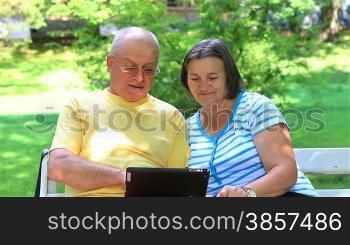 Senior couple sitting on a bench in the park and working on digital tablet pc