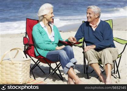 Senior Couple Sitting On Beach In Deckchairs Having Picnic