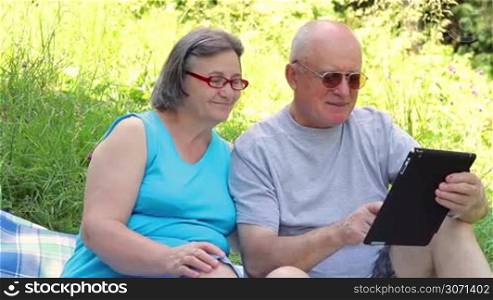 Senior couple sitting on grass working on digital tablet pc.